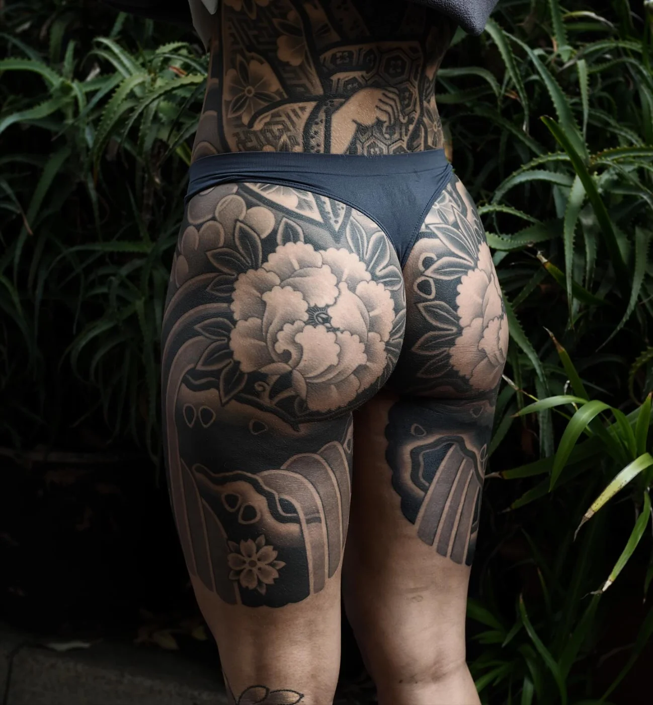 Large black-and-grey floral tattoo on a woman's thigh.