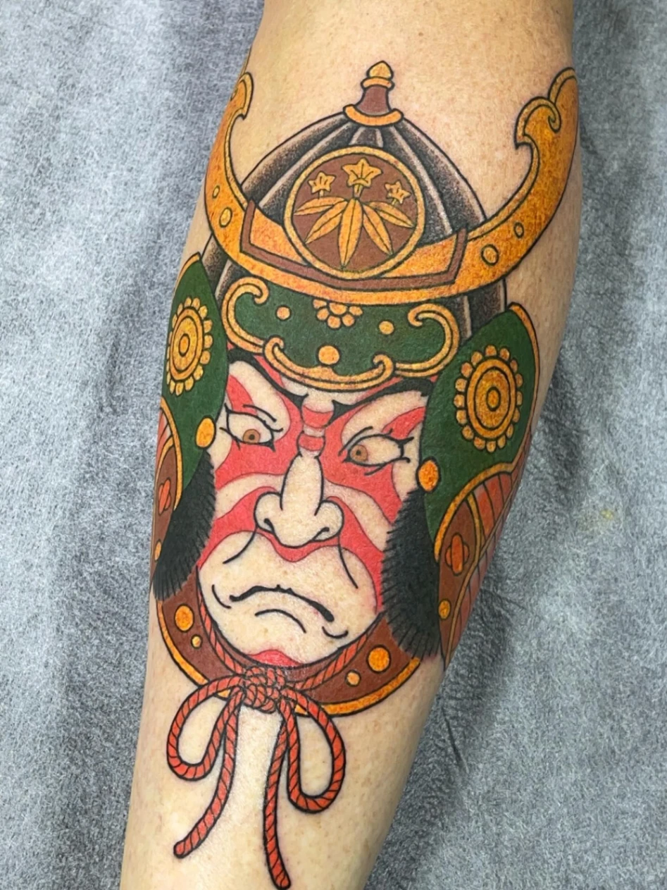 Traditional samurai tattoo on leg featuring a warrior's face.