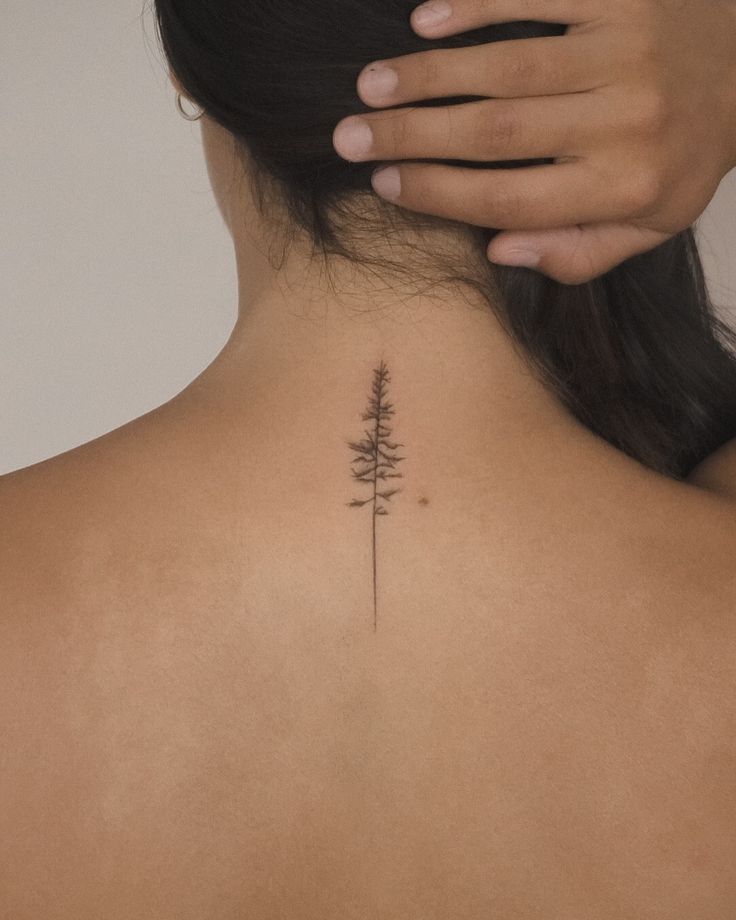 the back of a woman's neck with a small pine tree tattoo on it