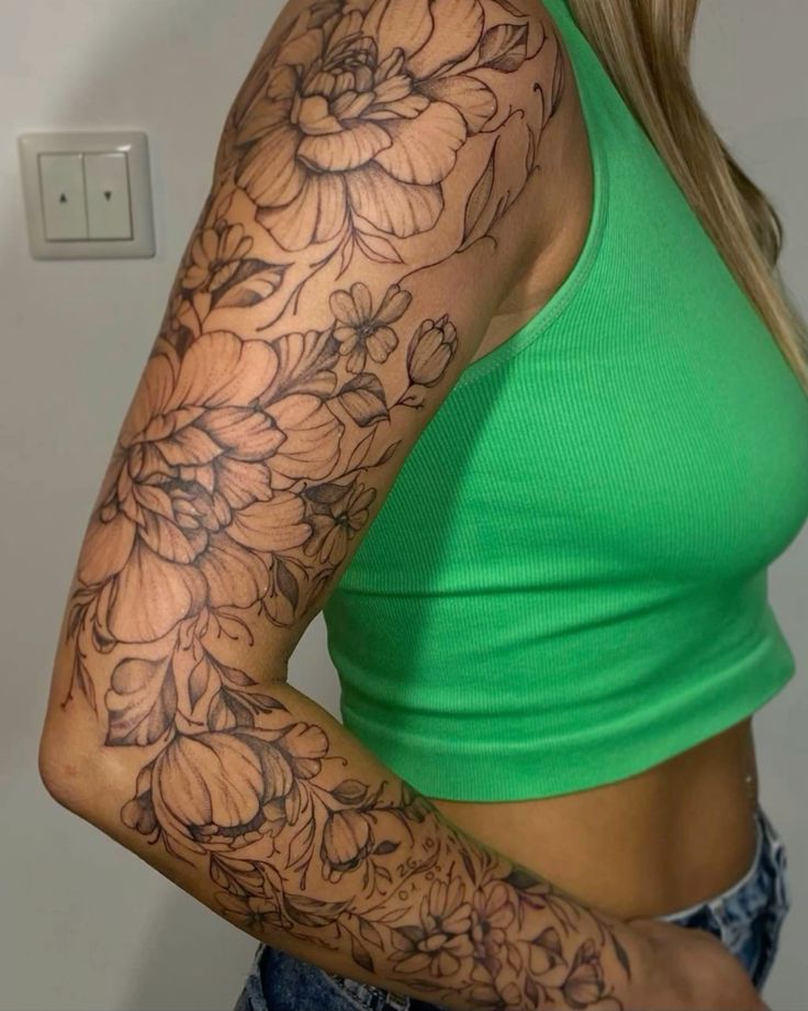 a woman's arm with flowers on it and a green tank top in the background